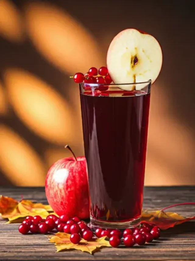 A festive glass of Autumn Cran-Apple Bliss, with a radiant crimson hue, garnished with fresh cranberries and a thin slice of apple.