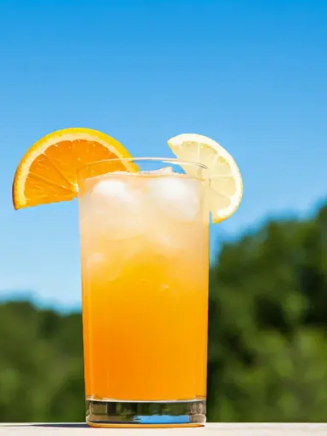 A vibrant glass of Zesty Citrus Elixir glowing with a sunny orange hue garnished with a lemon wheel and a sprig of fresh mint