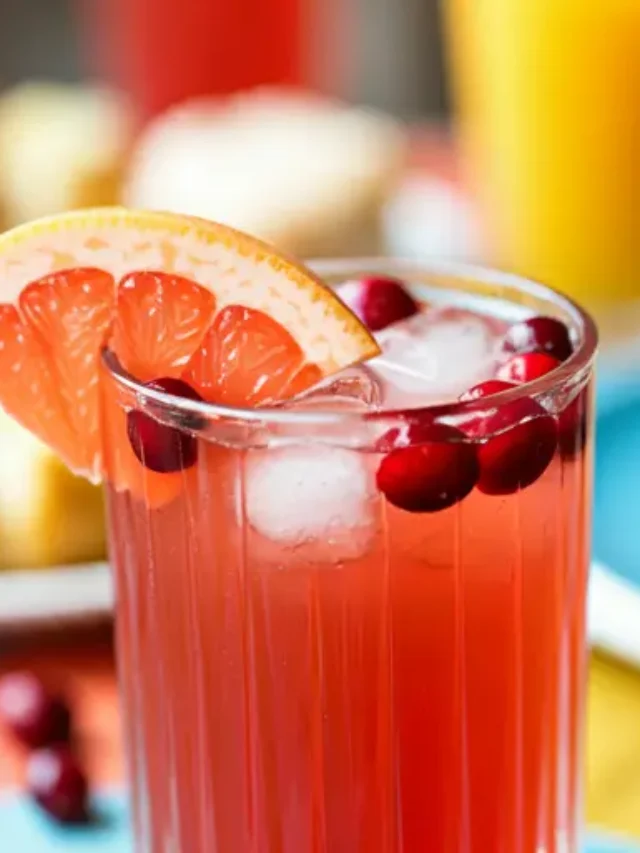 Ruby Sunrise Refresher : A vivid ruby-red juice in a glass, garnished with an orange wedge and a sprig of mint, exuding fresh and invigorating sunrise vibes.